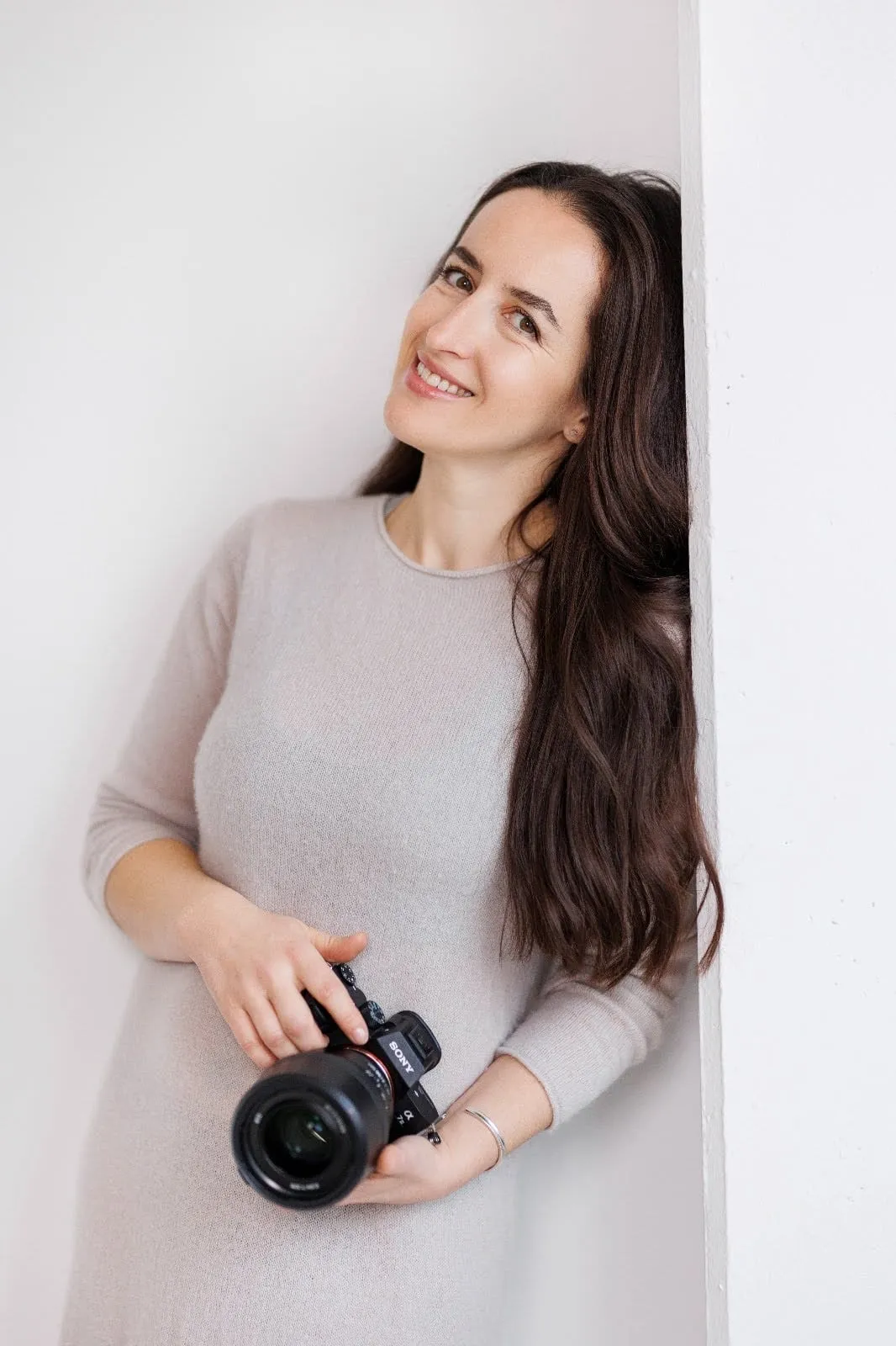 Tetyana Pirker, professionelle Hochzeitsfotografin in München, lächelndes Porträt mit Canon-Kamera im hellen Pullover